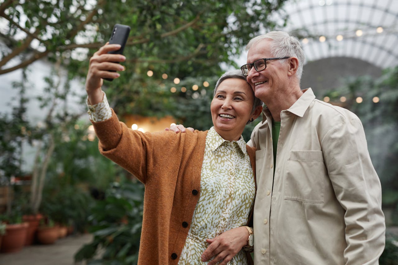 Happy senior couple taking a selfie in a lush garden setting, capturing a joyful moment.