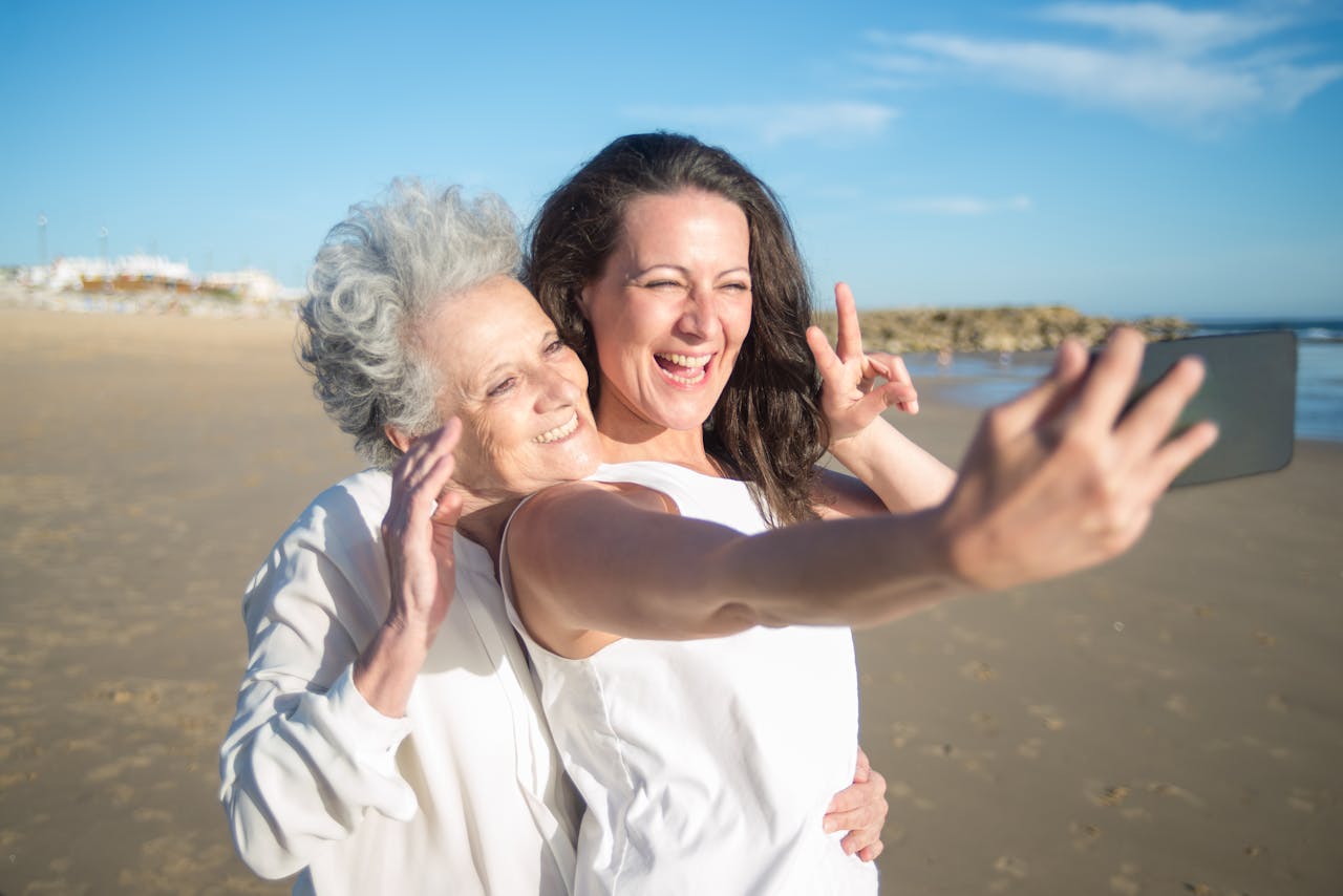 Elderly and adult woman take a joyful selfie on the sunny beach in Portugal, showcasing love and connection.